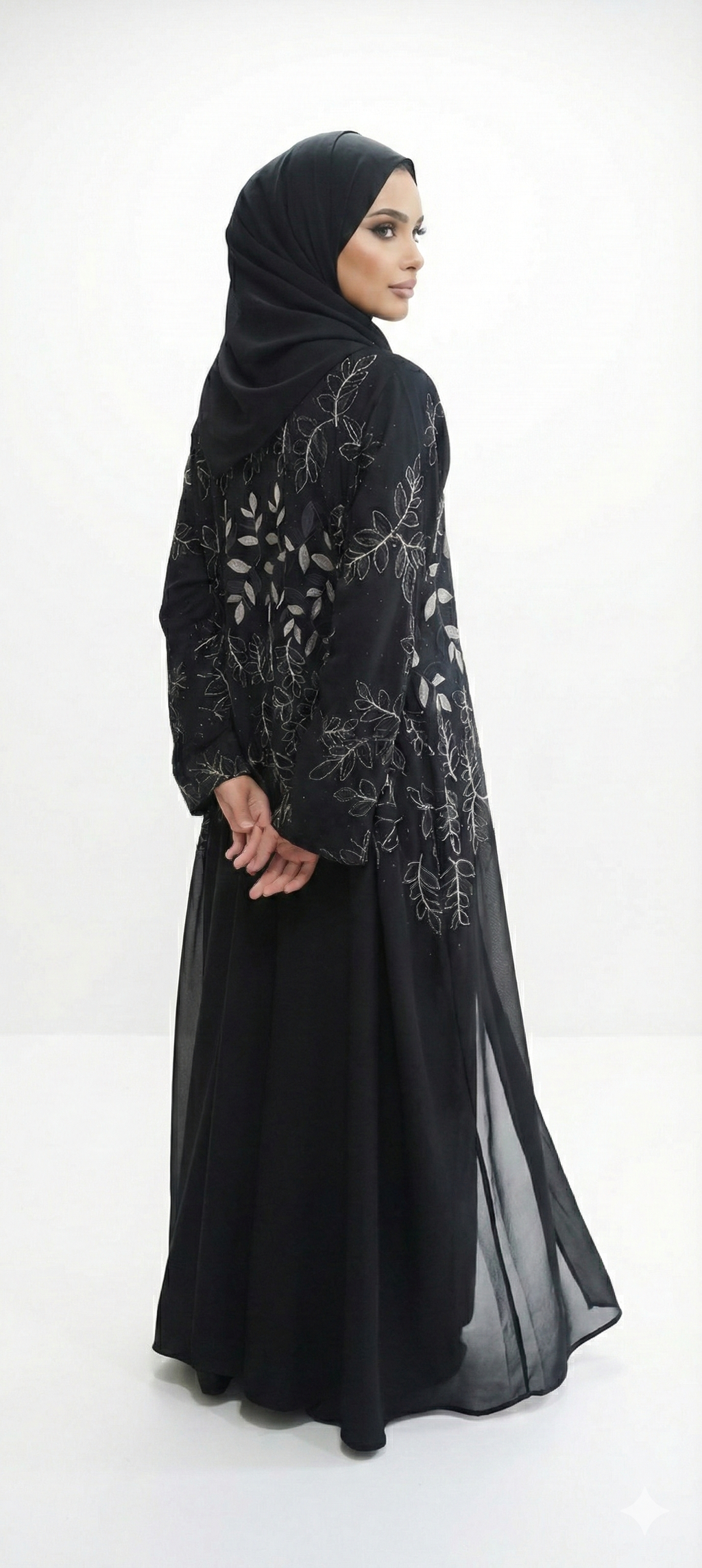 Back/side view of black abaya with gold leaf embroidery and black leaf detailing, model turning slightly to show the design.