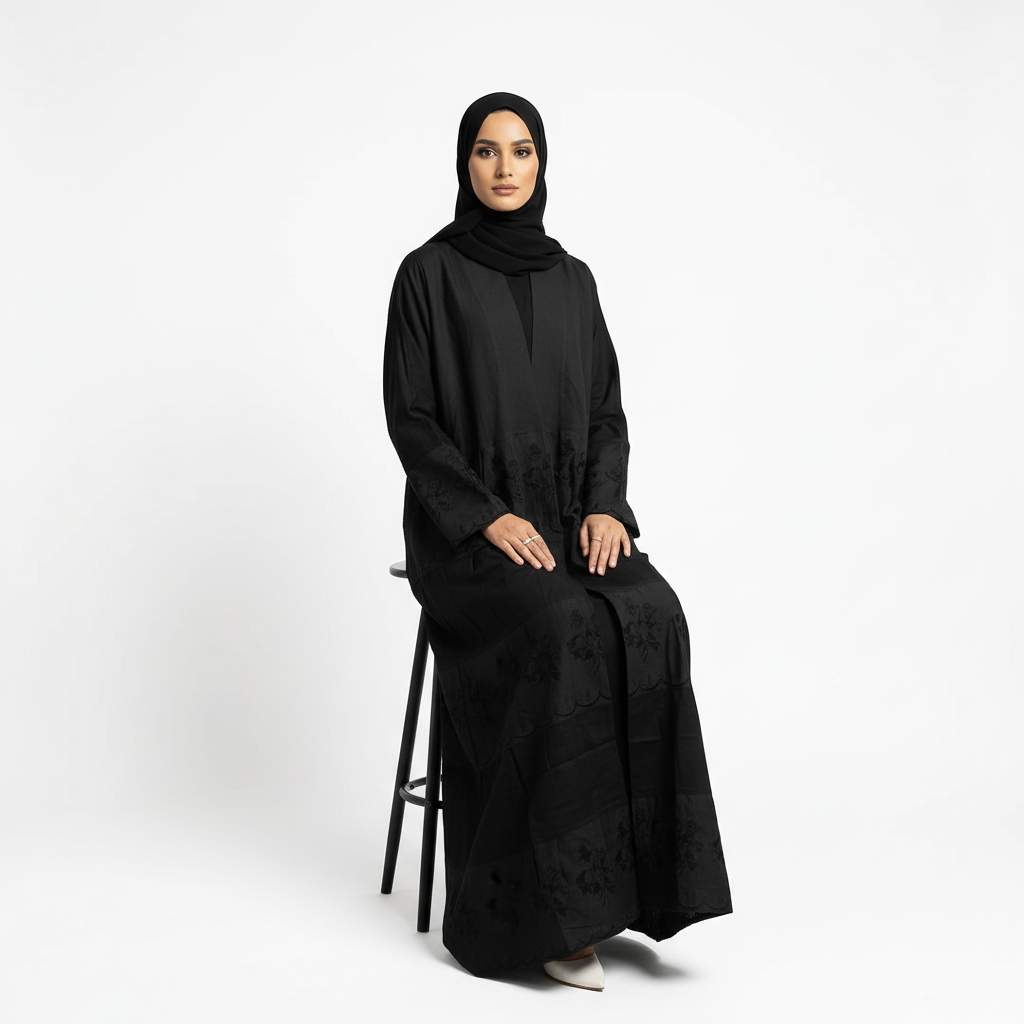 Seated pose in black Hana layered crepe abaya with black-on-black floral embroidery detail and matching black hijab.